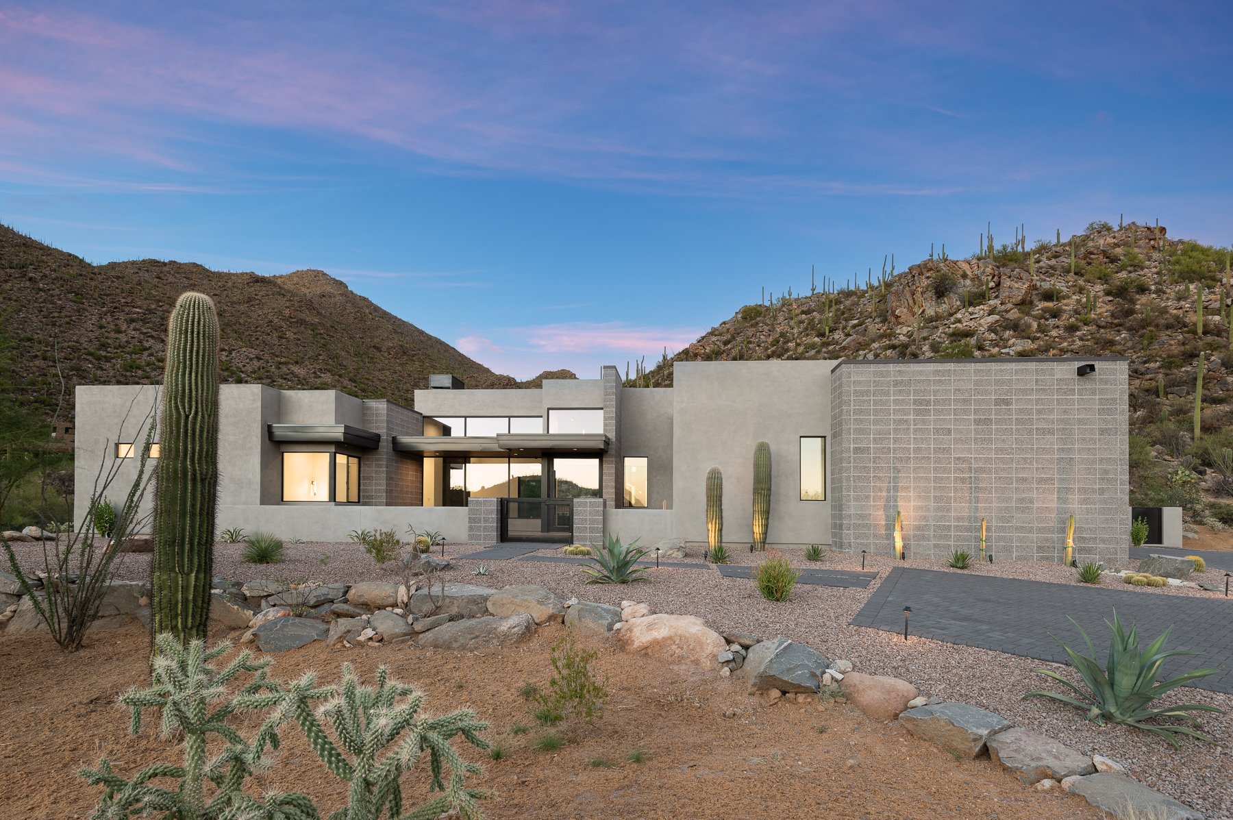 Modern desert home with cacti and mountainous backdrop at sunset.