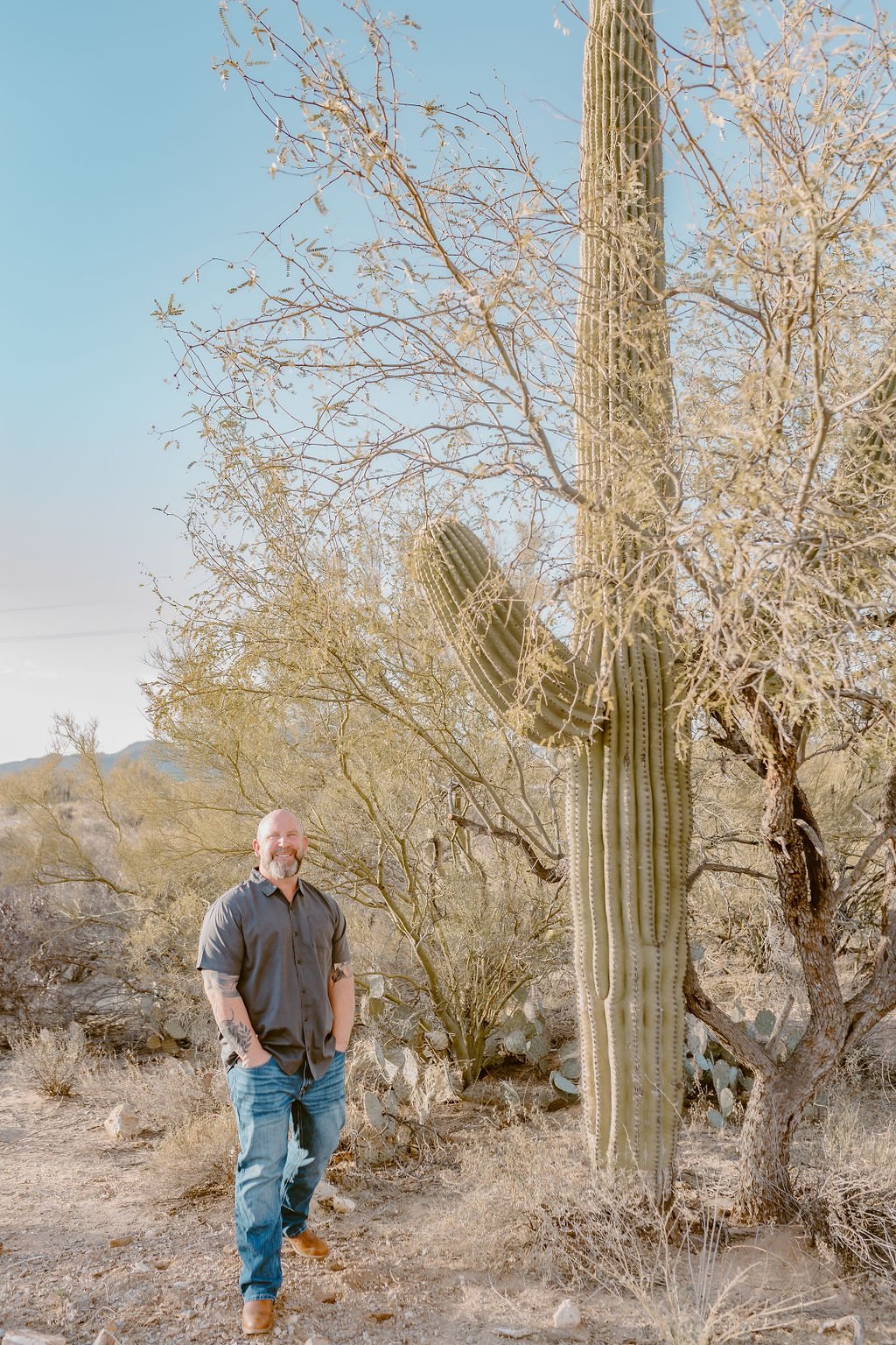 Man standing next to a large saguaro cactus in a desert landscape.