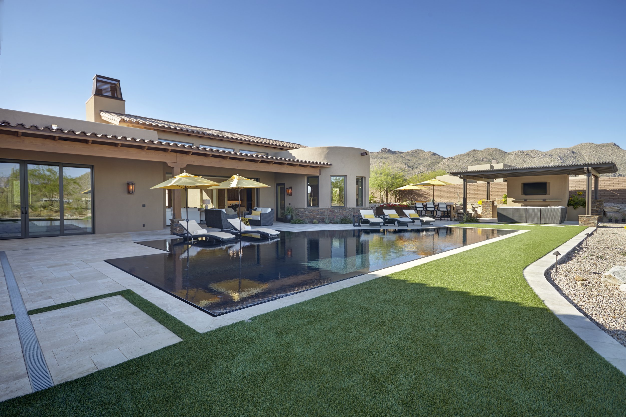 Luxury backyard with pool, lounge chairs, and patio umbrellas in a desert setting.
